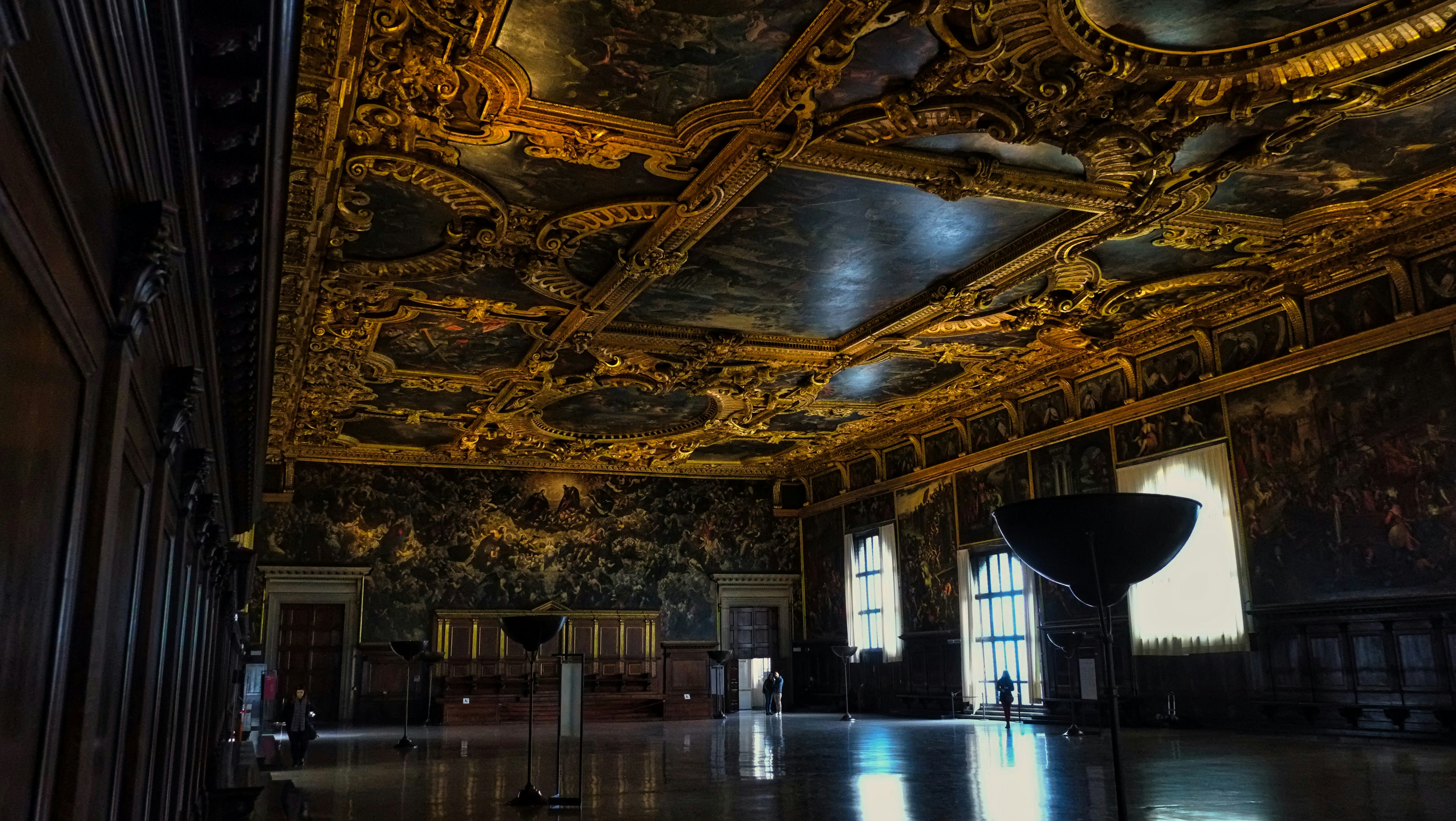 A grand hall with a gilded painted ceiling, large windows, and dark wood paneling.