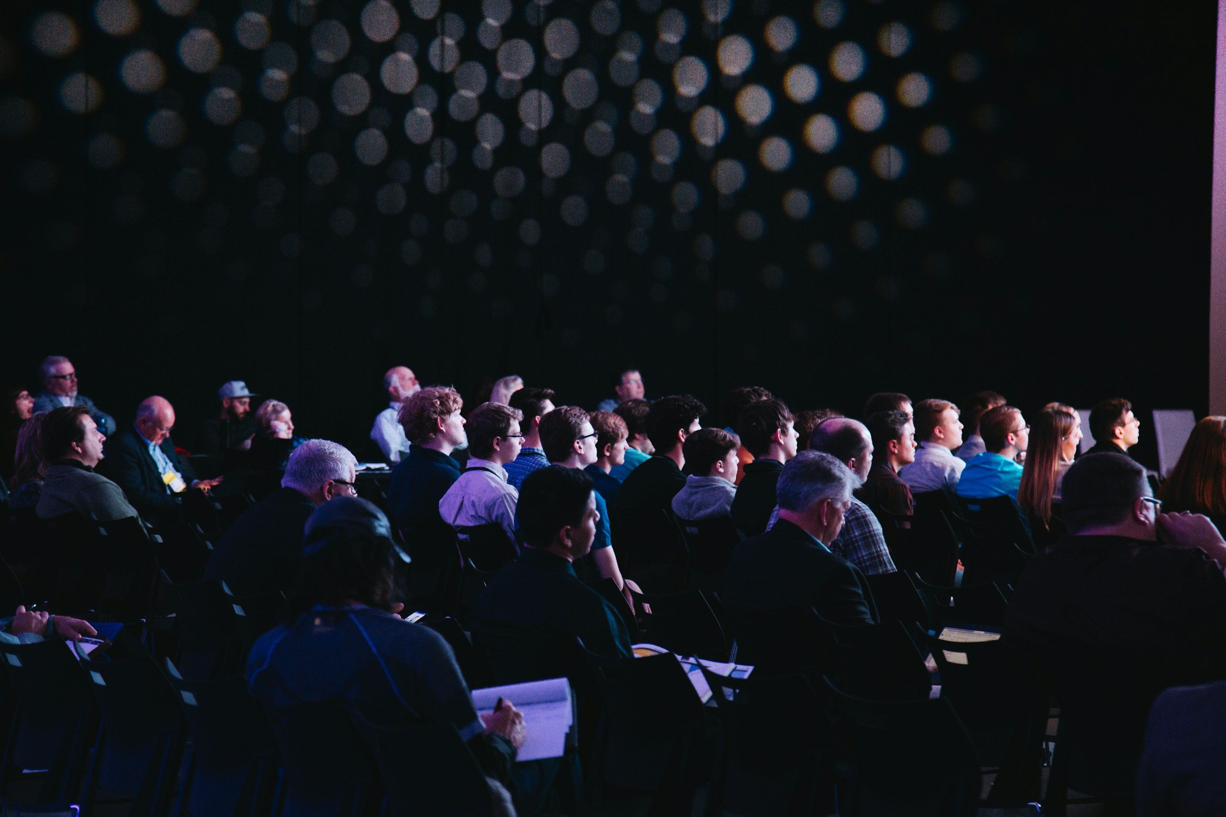 Audience seated in dark room watching a presentation or event.