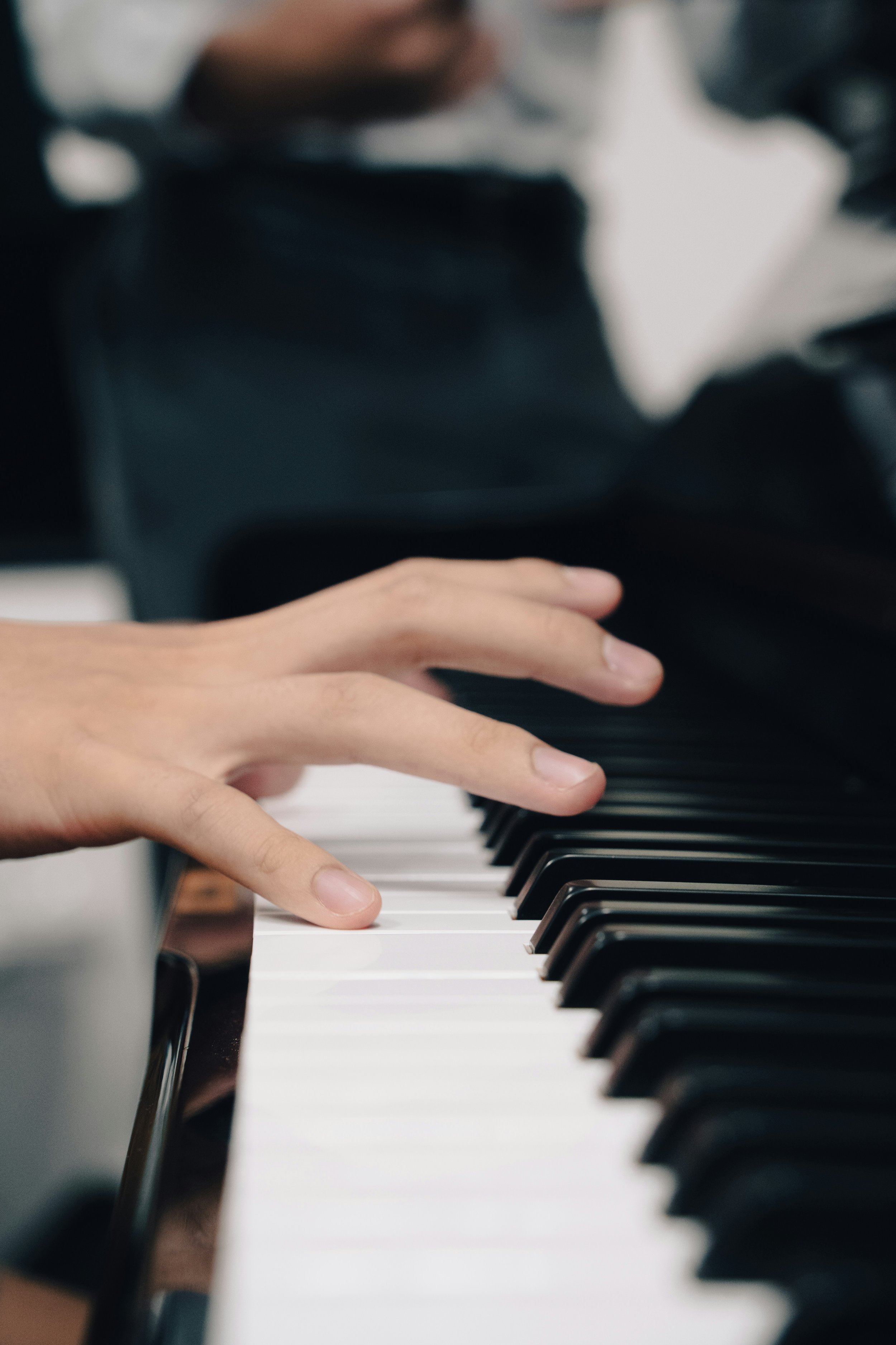 Close-up of a person's hand playing piano keys with a blurred background.