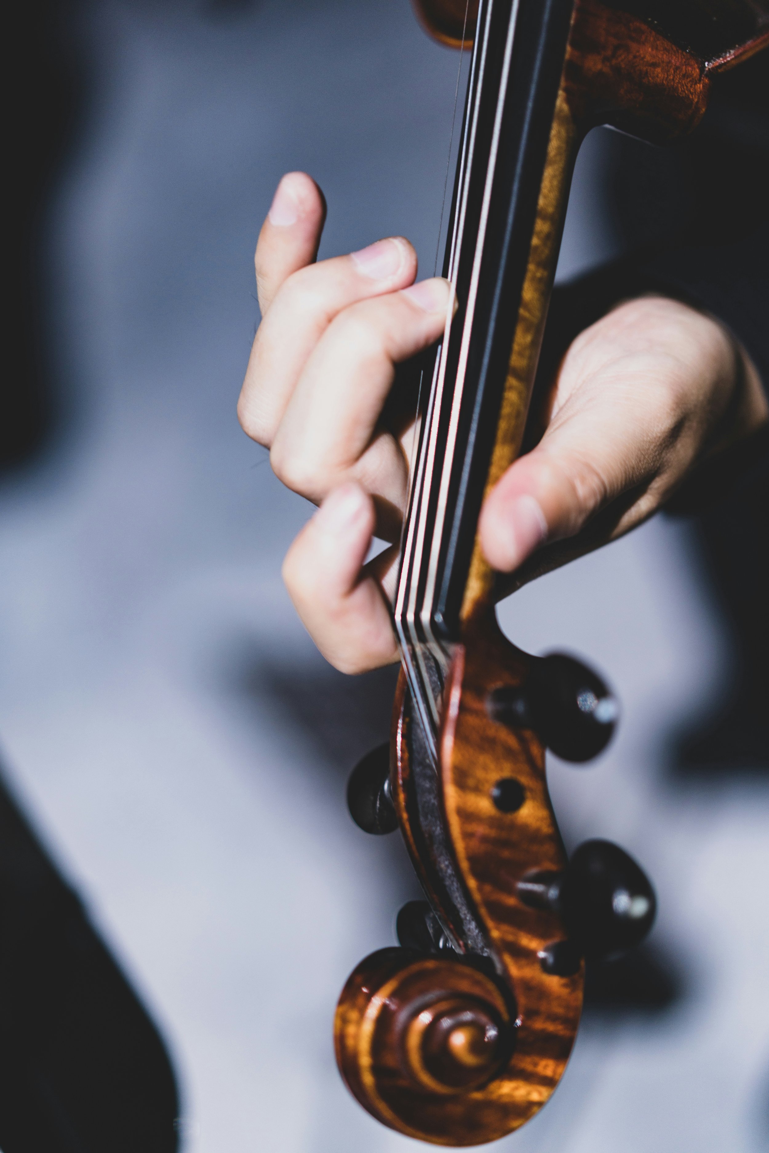 Close-up of a person's hand playing a violin, focusing on the finger pressing the strings on the fingerboard.